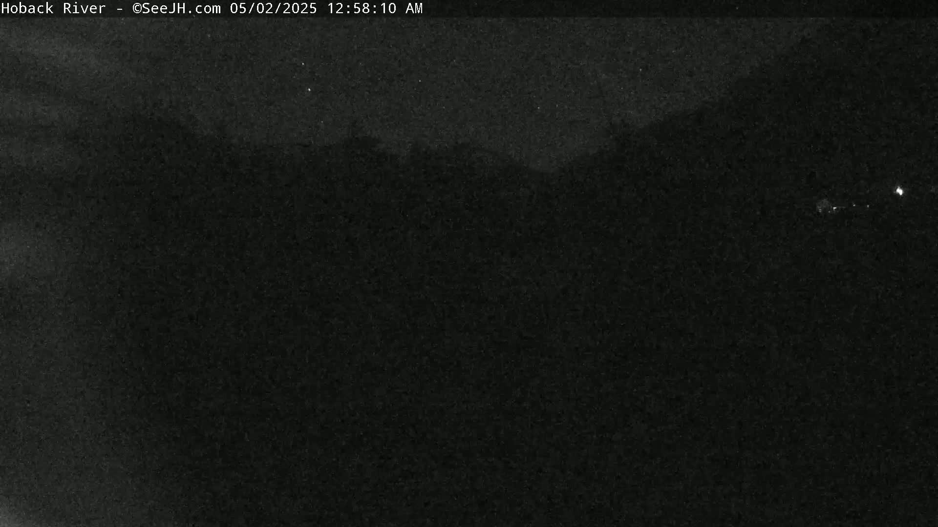 A nighttime, low-light image shows a dark, indistinct landscape under a clear, starry sky.