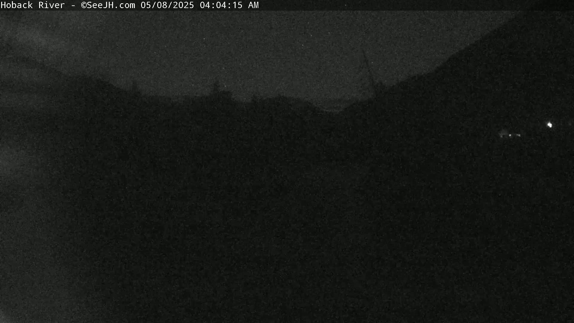 A nighttime, low-light view of a dark landscape with faint, distant lights.
