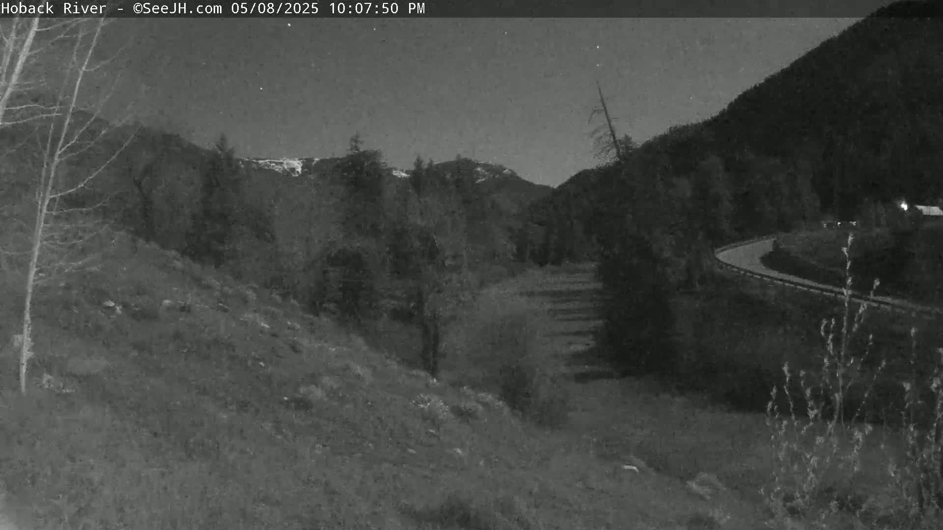 A nighttime view of a winding road curving through a mountainous landscape under a dark, clear sky.