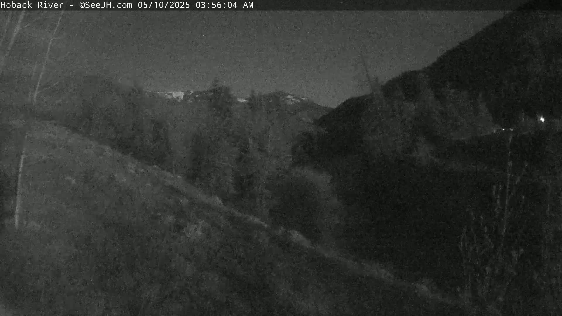 A nighttime view of a dark, sloped hillside leading to a mountain range under a clear, dark sky.