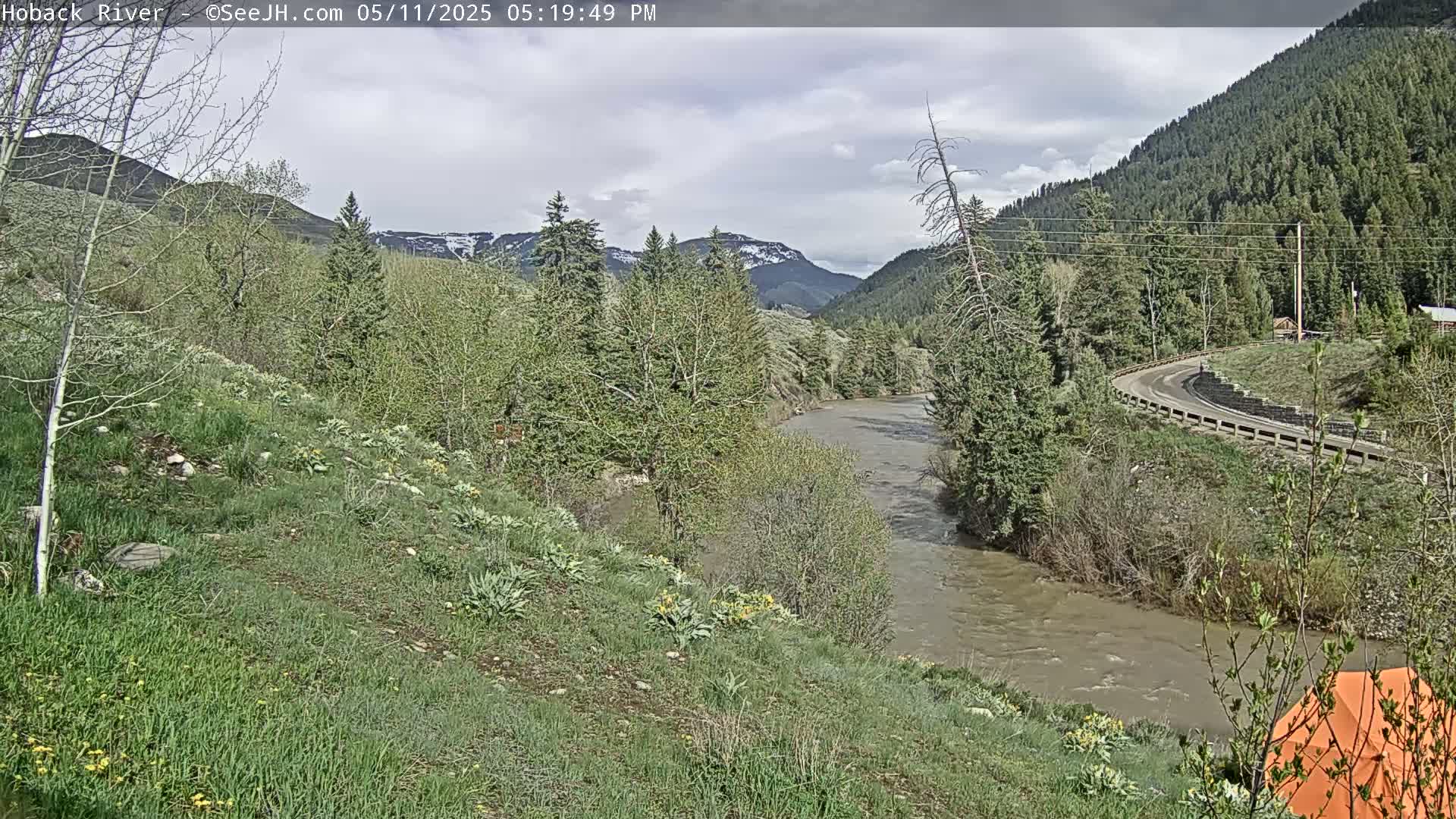 A muddy river flows through a valley of green trees and hills under a partly cloudy sky.