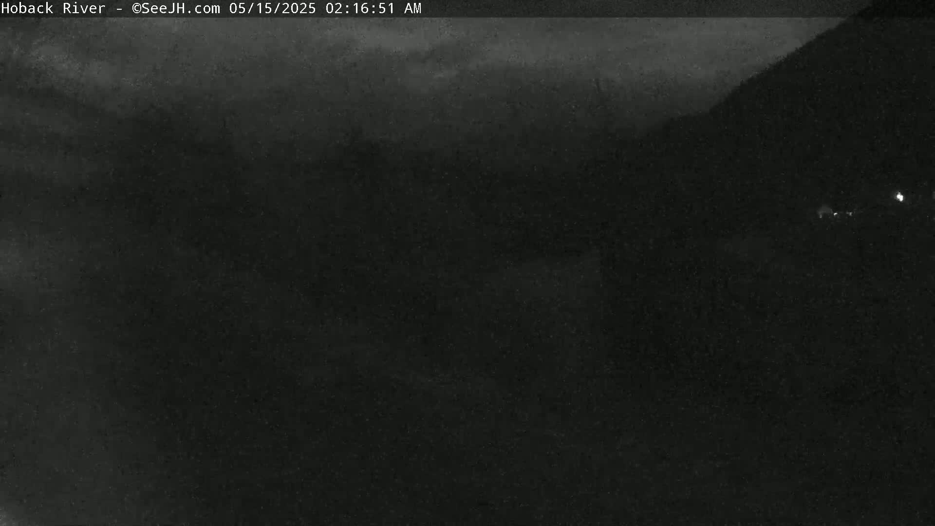 A dark, nighttime outdoor scene shows a mostly obscured view of a landscape under a cloudy sky.