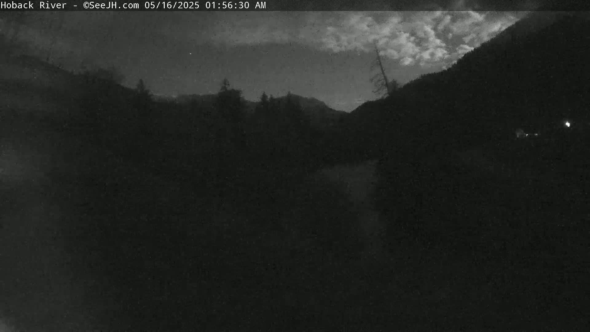 A nighttime, cloudy view of a dark, wooded area with a body of water in the center.