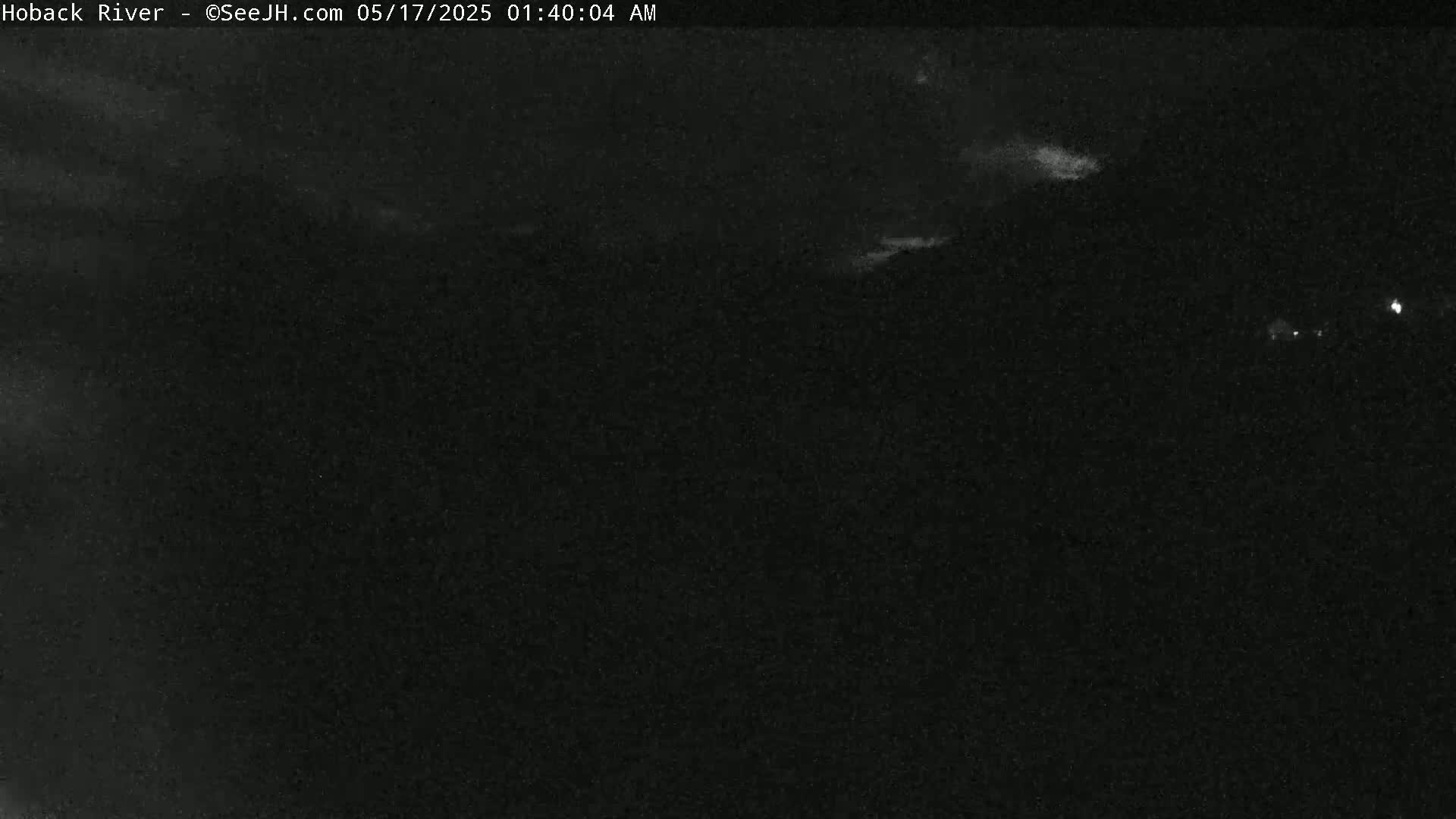 A nighttime, overcast view shows a dark landscape with faint light sources in the distance.