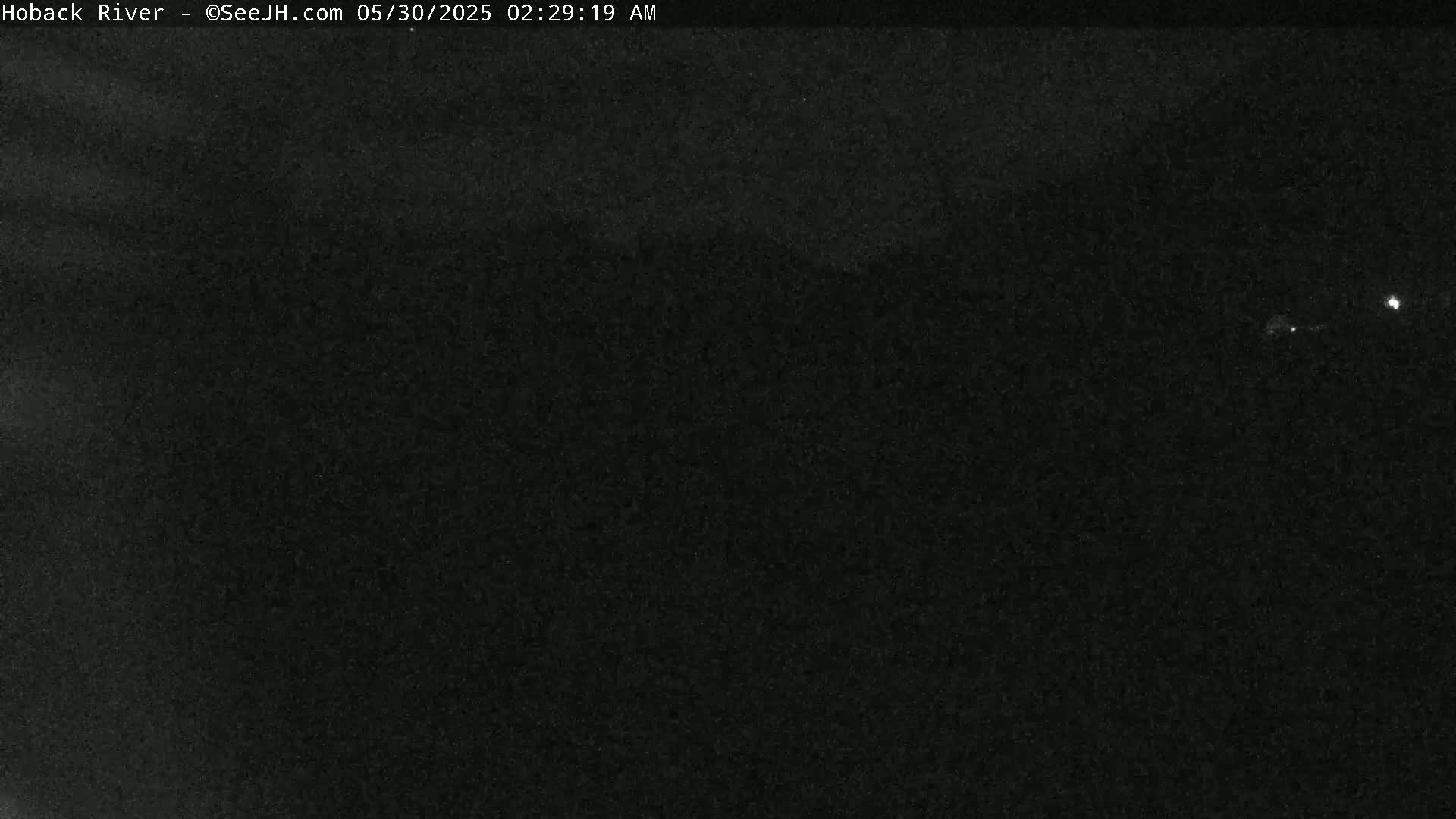 A nighttime, dark image shows a very faint, blurry view of possibly a river or landscape under a dark sky with a few distant lights visible.