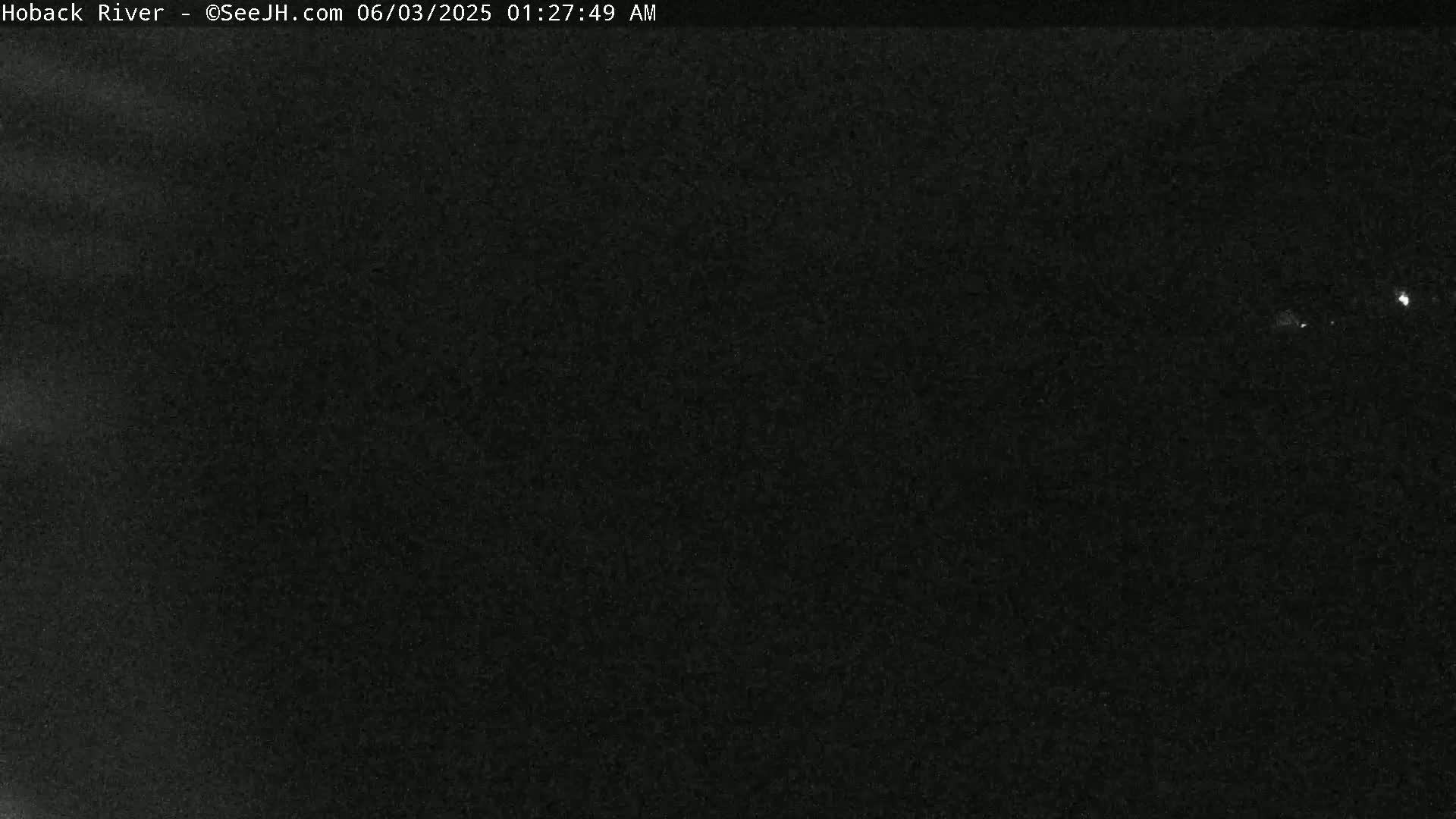 A dark, nighttime scene shows a mostly black, grainy image with a few faint, distant lights.