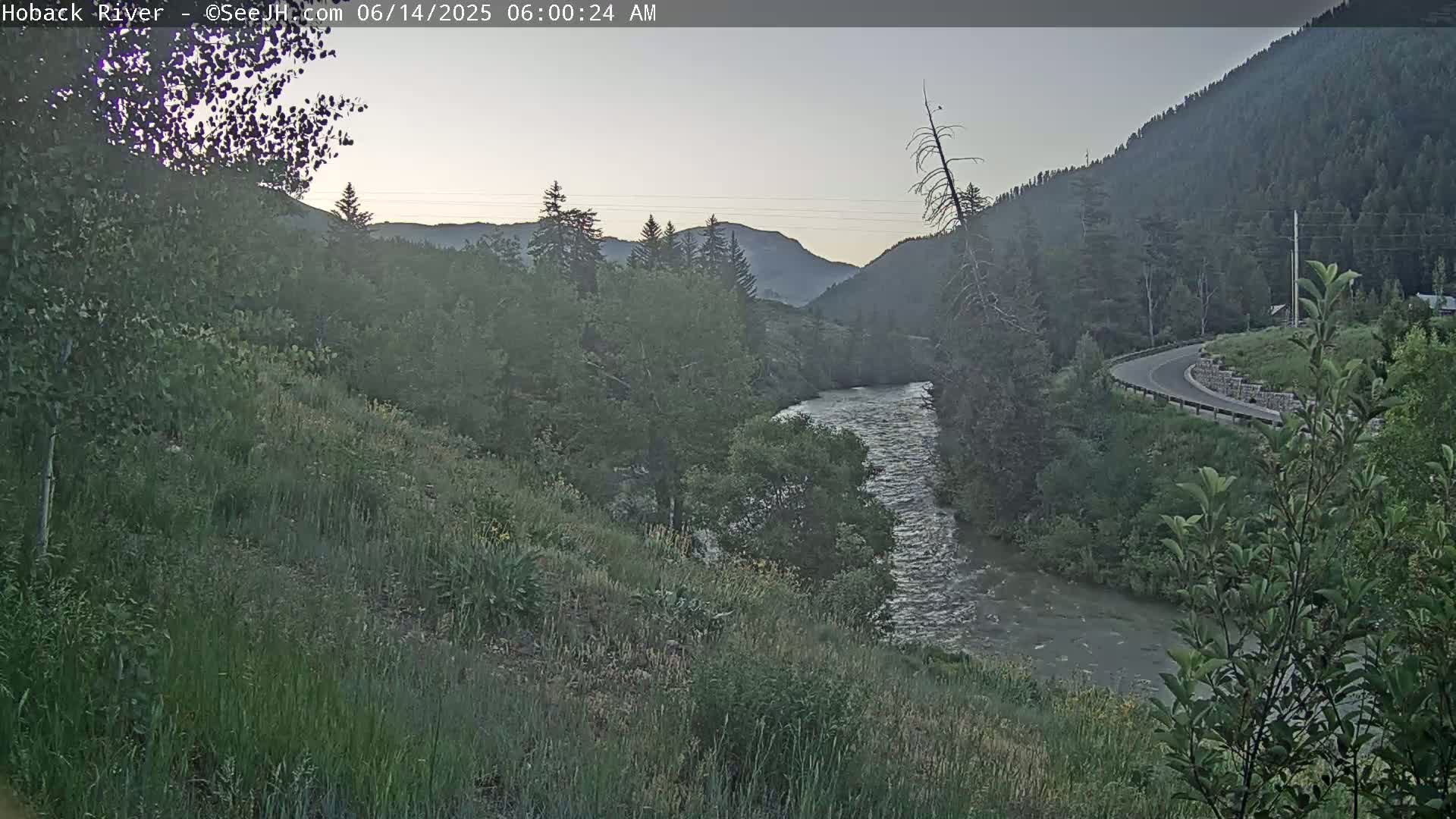 A river flows through a valley surrounded by green mountains under a dawn sky.