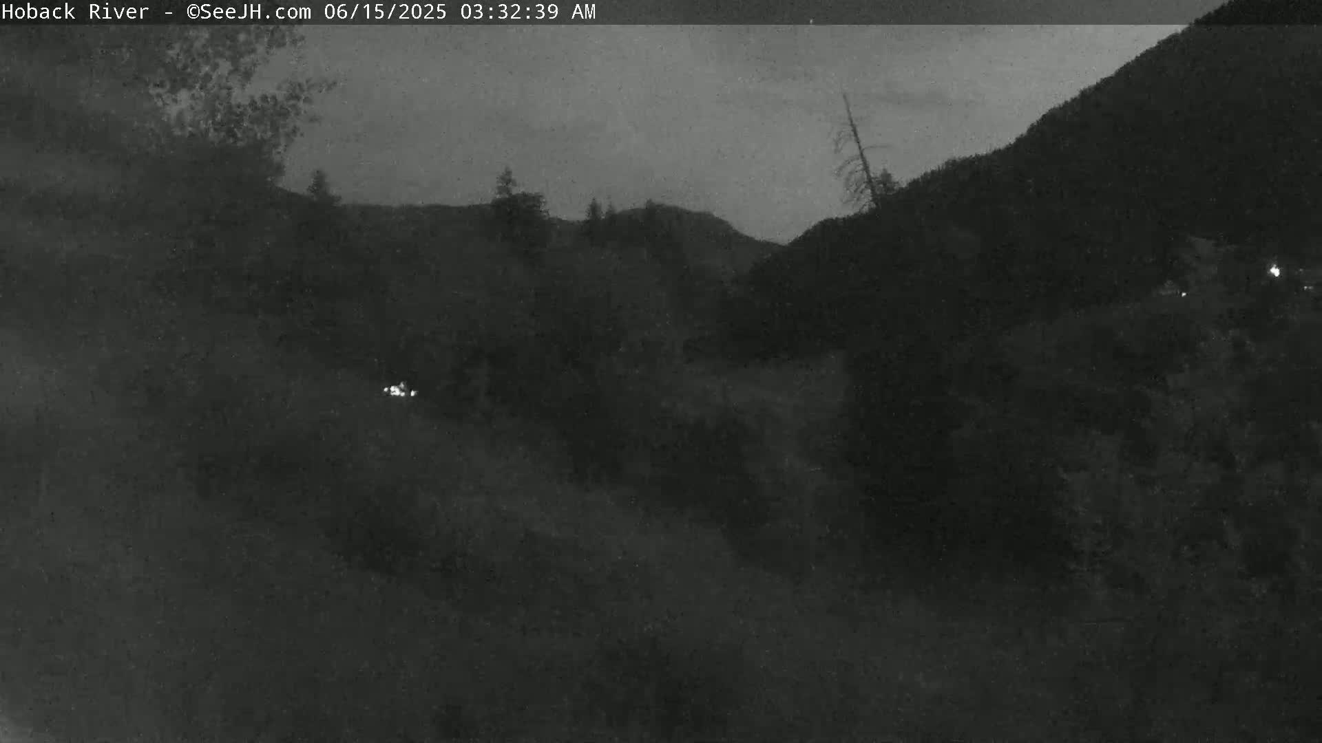 A dark, nighttime view of a hilly landscape with sparse vegetation under a mostly clear sky.