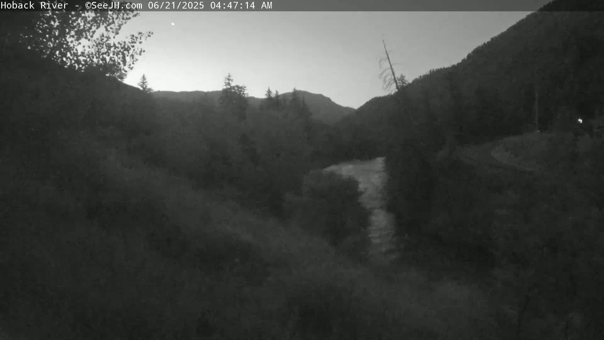 A dark, pre-dawn view of a river flowing through a mountainous valley.