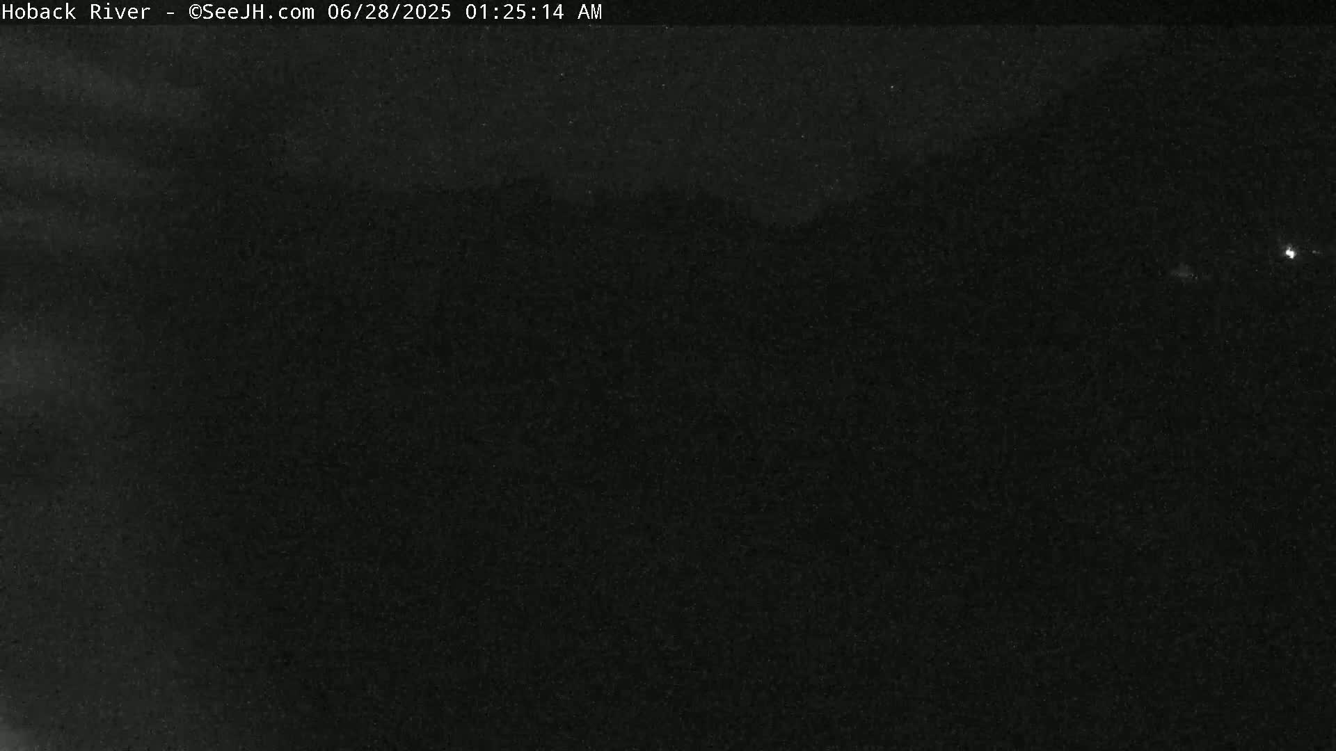 A dark, nighttime image shows a mostly black scene with faint light sources in the distance.
