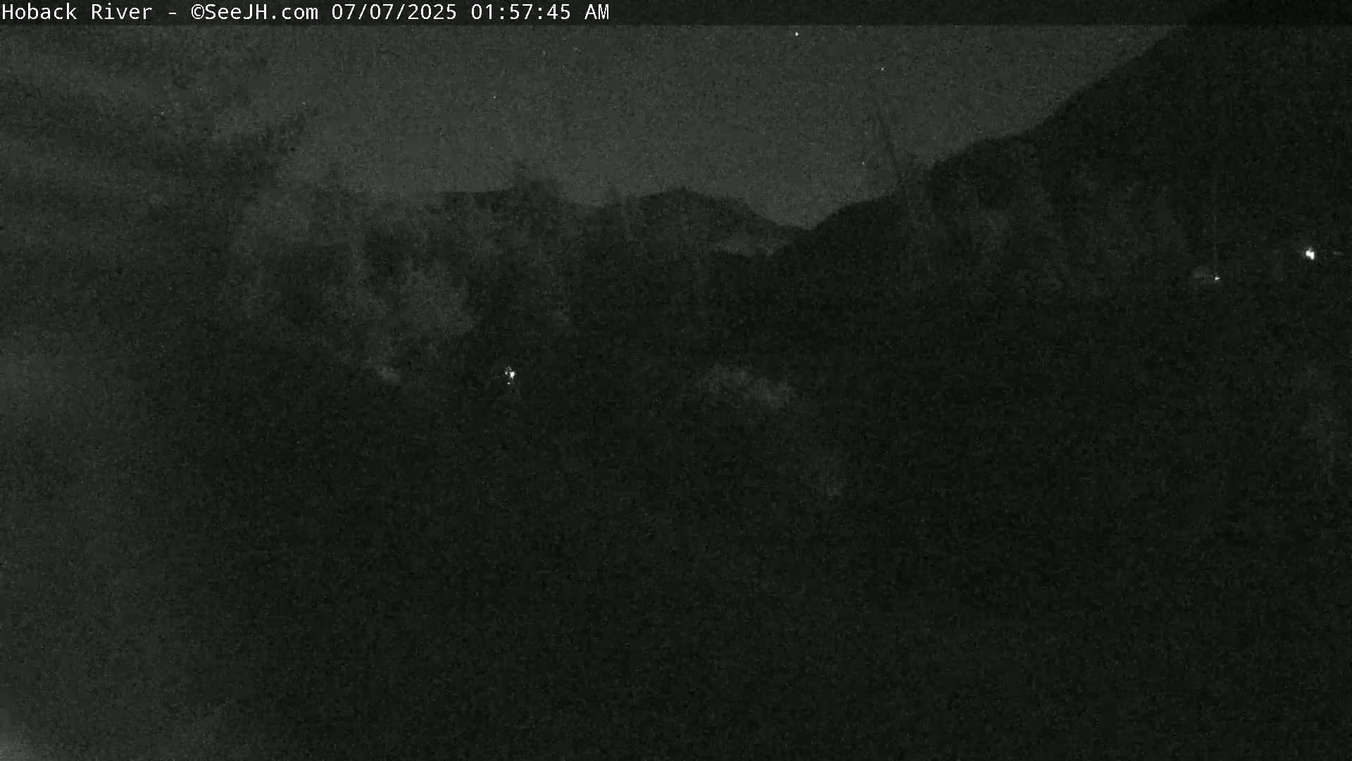 A nighttime, low-light view of dark, indistinct landforms under a clear, starry sky.