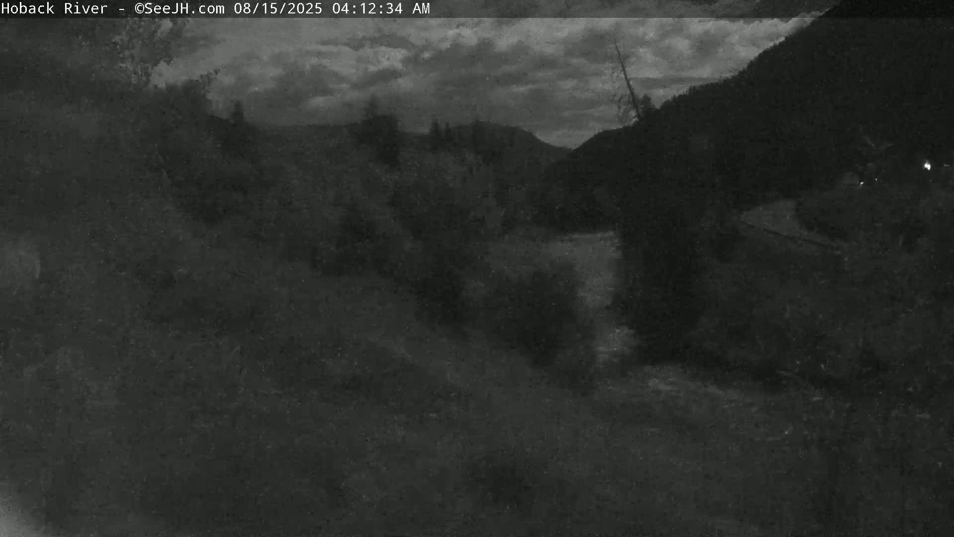 A dark, nighttime image shows a few faint lights in the distance against a mostly black sky.