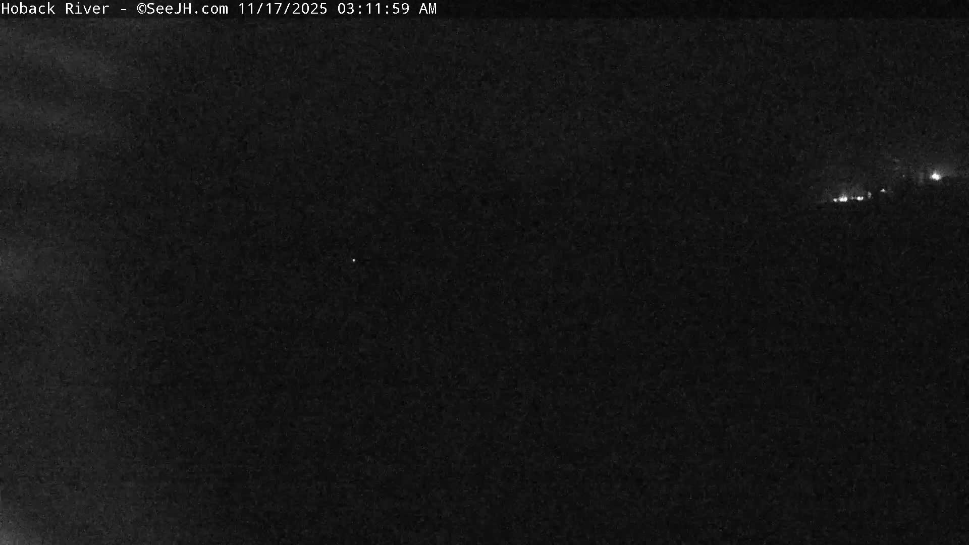 A very dark outdoor scene at night with clear weather, showing only a few faint distant lights on the right horizon.