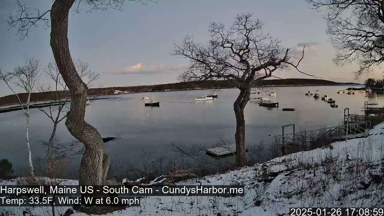 A snow-dusted shoreline overlooks a calm bay with several boats, under a twilight sky.