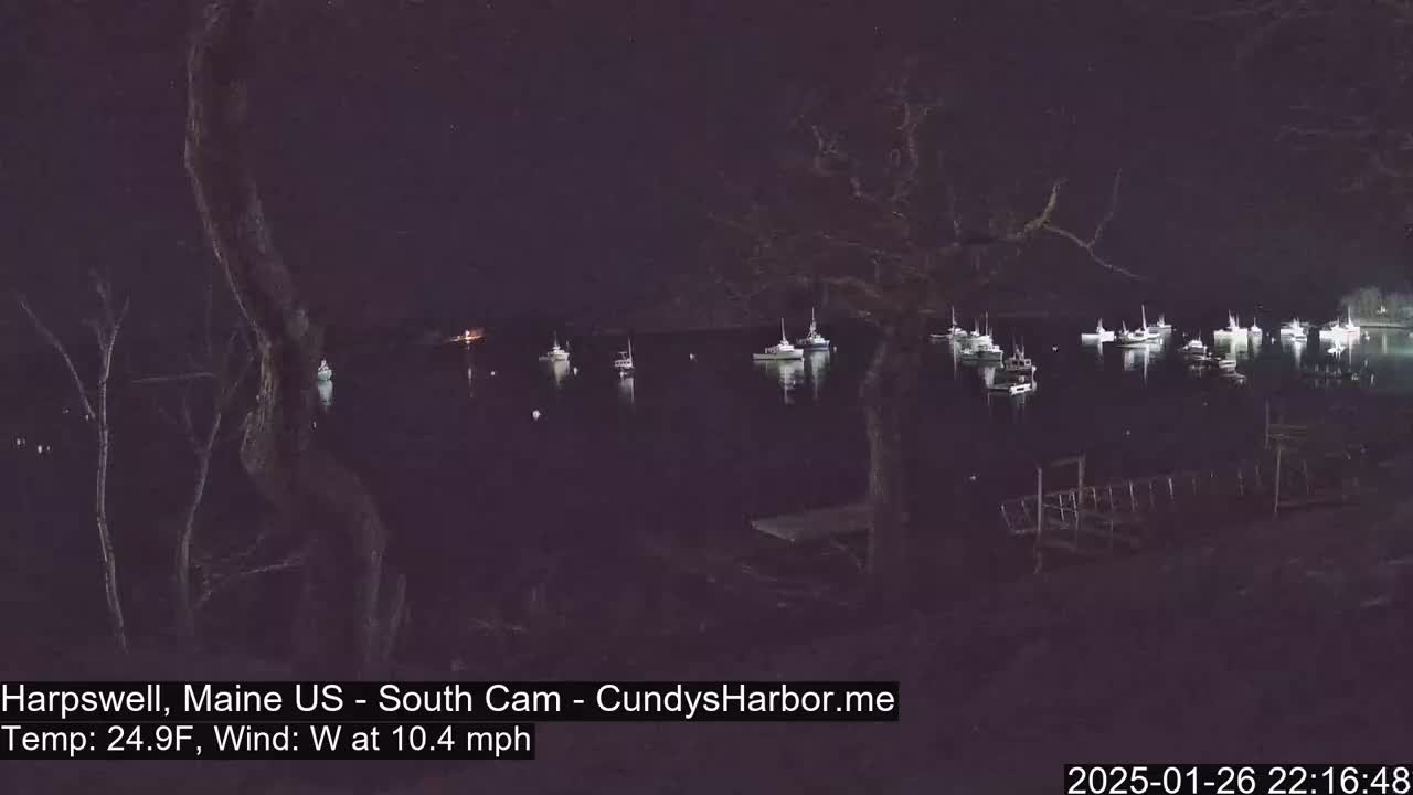 At night, a calm body of water is dotted with numerous boats under a dark sky with a westerly wind at 10.4 mph and a temperature of 24.9°F.