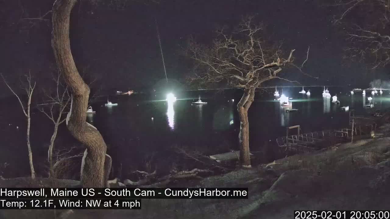 Several boats are moored in a dark harbor at night under a clear sky, with a northwest wind blowing at four miles per hour and a temperature of twelve point one degrees Fahrenheit.