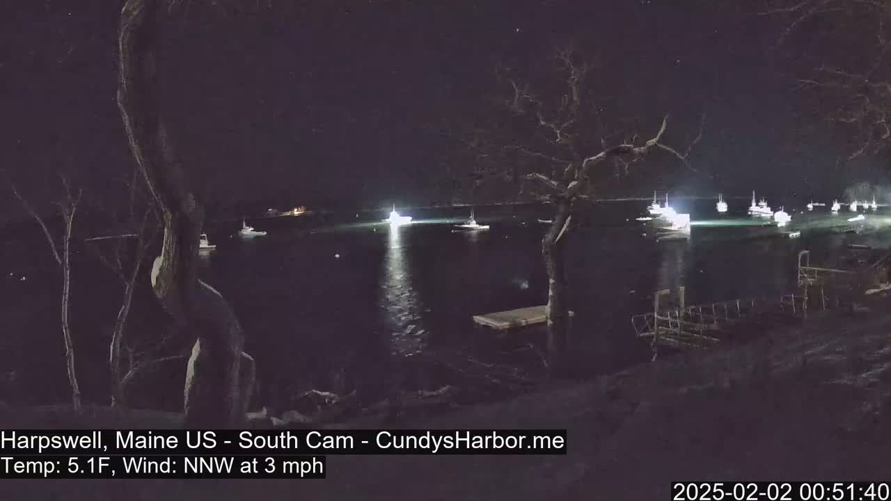 Several boats are illuminated in a dark harbor at night under a clear, starry sky with a light northwest wind.