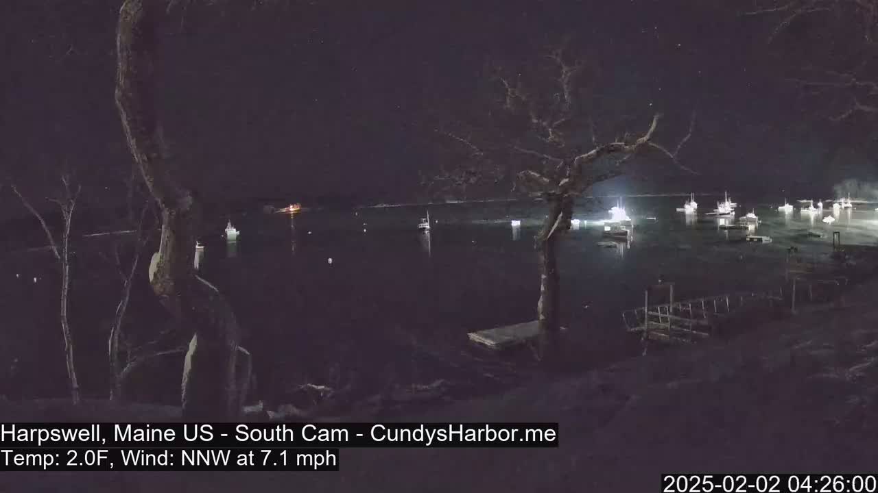 A nighttime view of a harbor with numerous boats, under a starry sky with a north-northwest wind at 7.1 mph and a temperature of 2 degrees Fahrenheit.