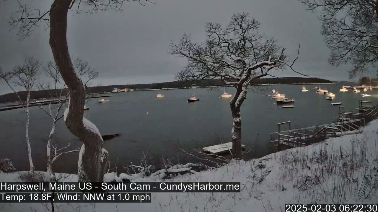 A snow-covered shoreline overlooks a calm harbor filled with numerous boats at twilight.