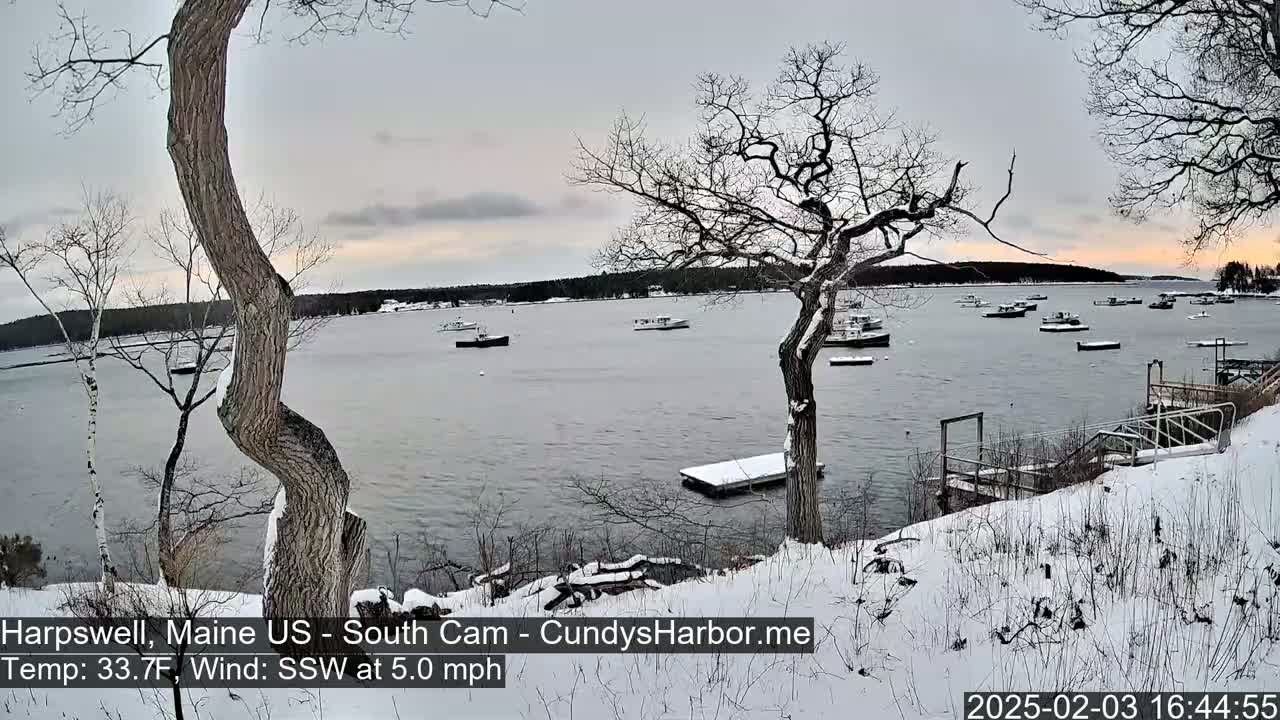 A snow-covered shoreline with several boats in a calm bay under a twilight sky.