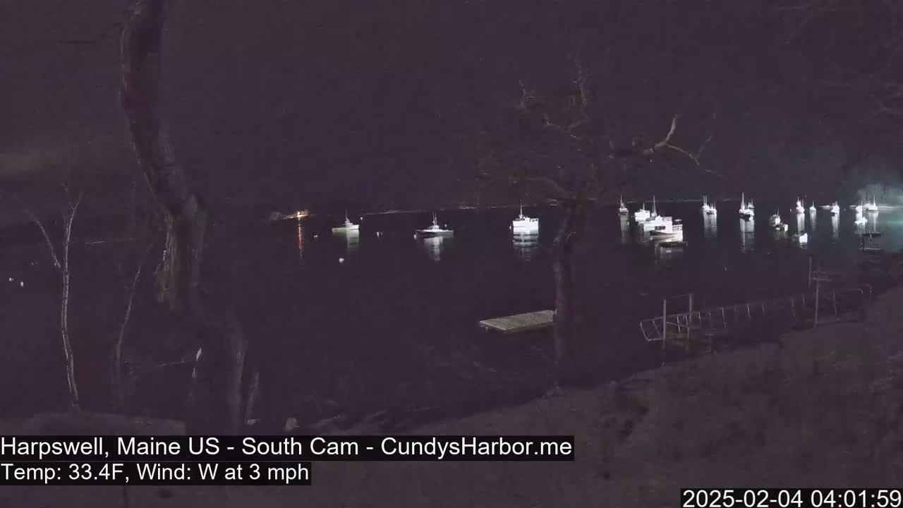 Several boats are moored in a dark harbor at night, under a clear sky with a 3 mph westerly wind and a temperature of 33.4°F.