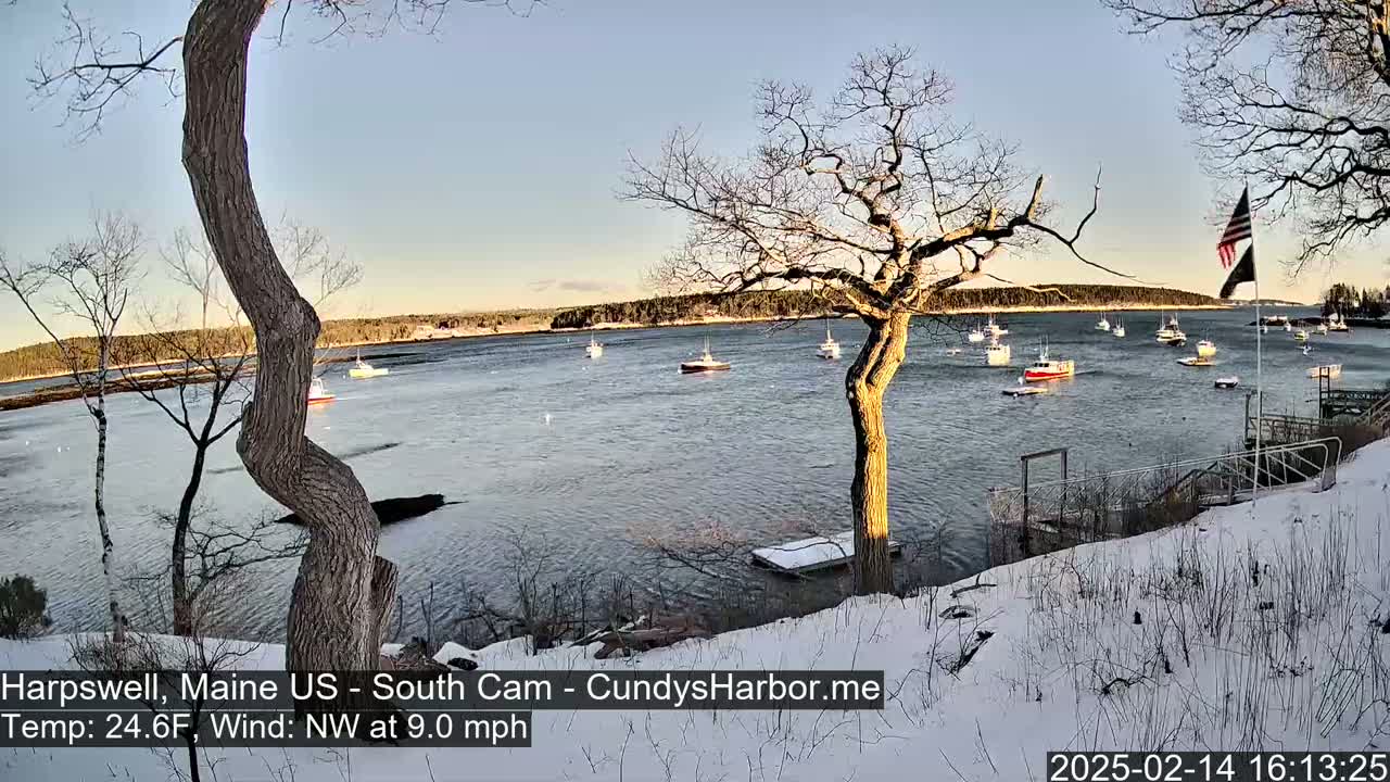 A snow-covered shoreline with several boats in a calm body of water under a clear, twilight sky.