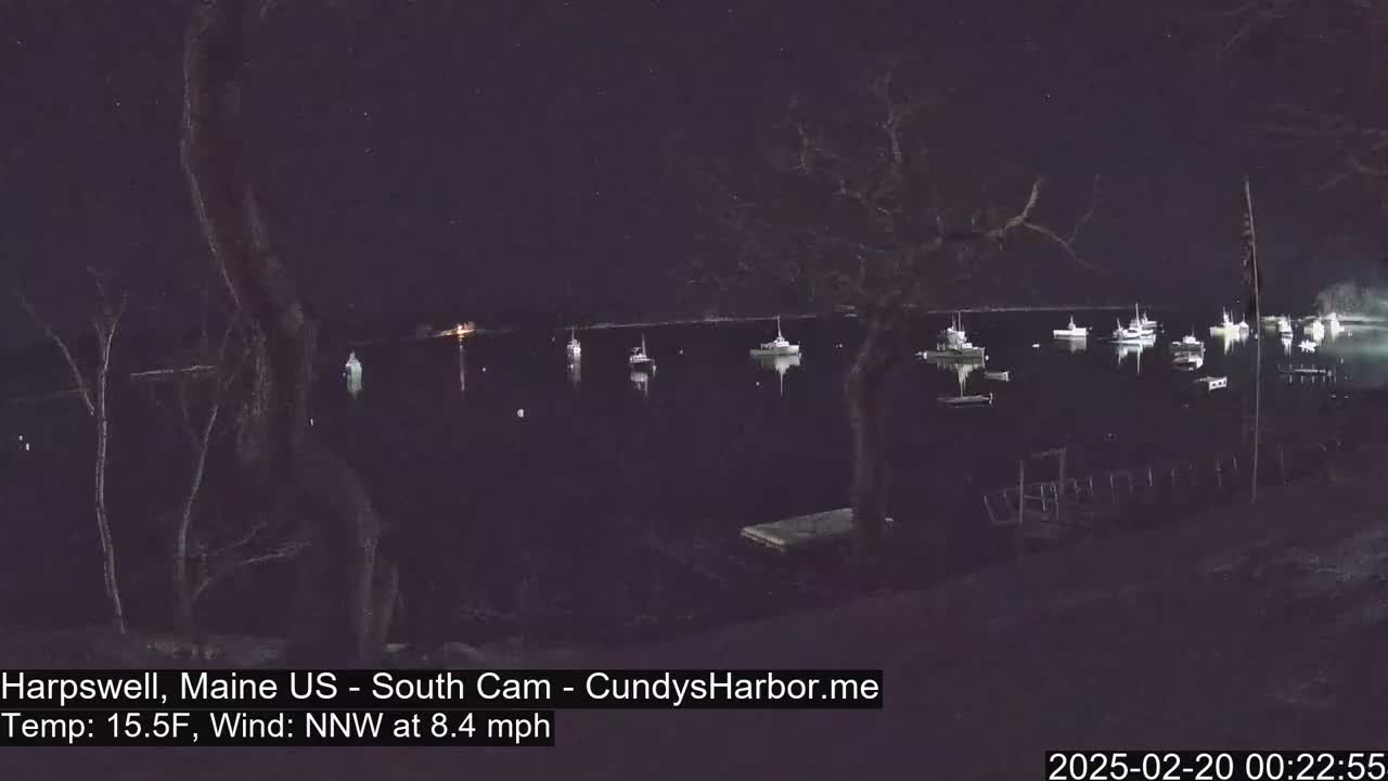 A nighttime view of a calm body of water with several boats moored, under a starry sky and a 15.5°F temperature with a northwest wind.