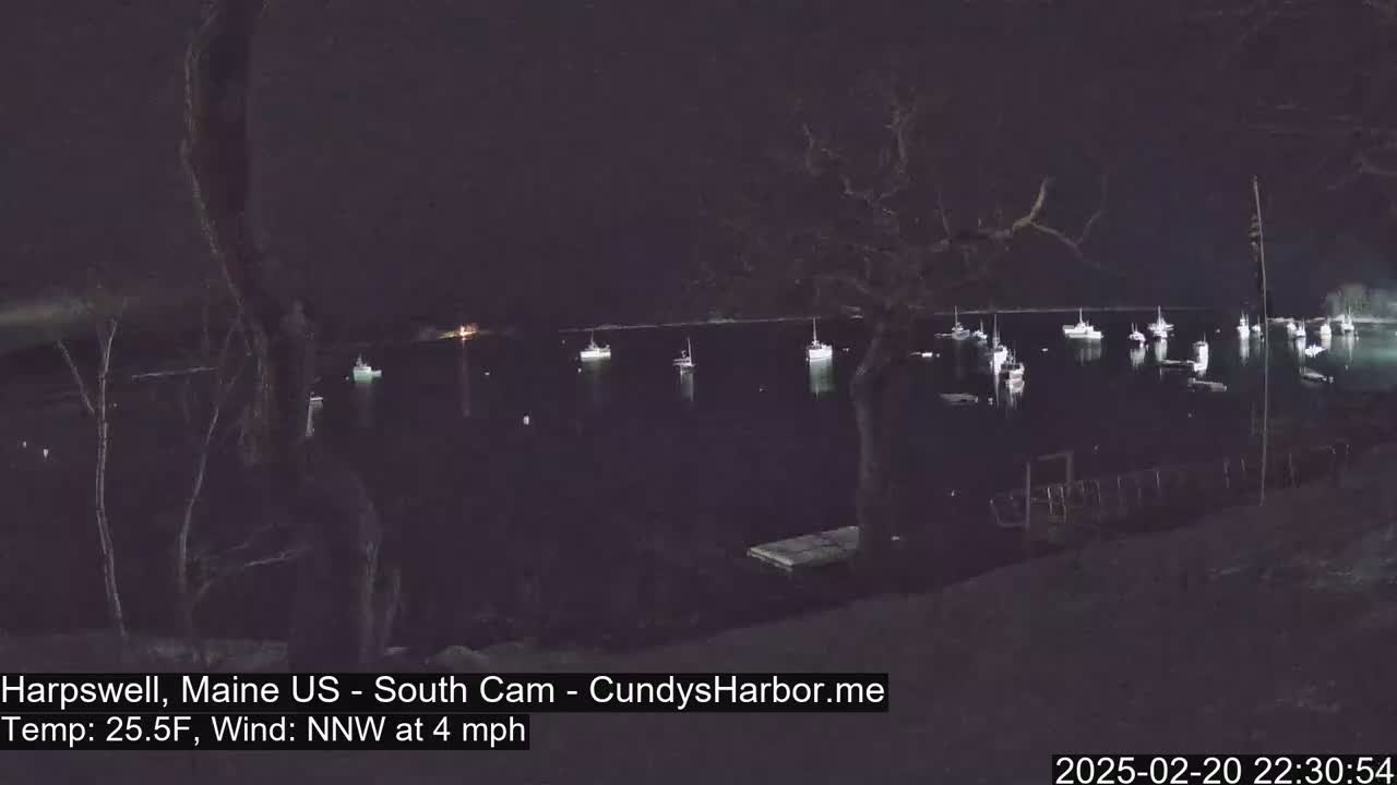 A nighttime view of a harbor with numerous boats at anchor under a dark sky, with a light north-northwest wind.