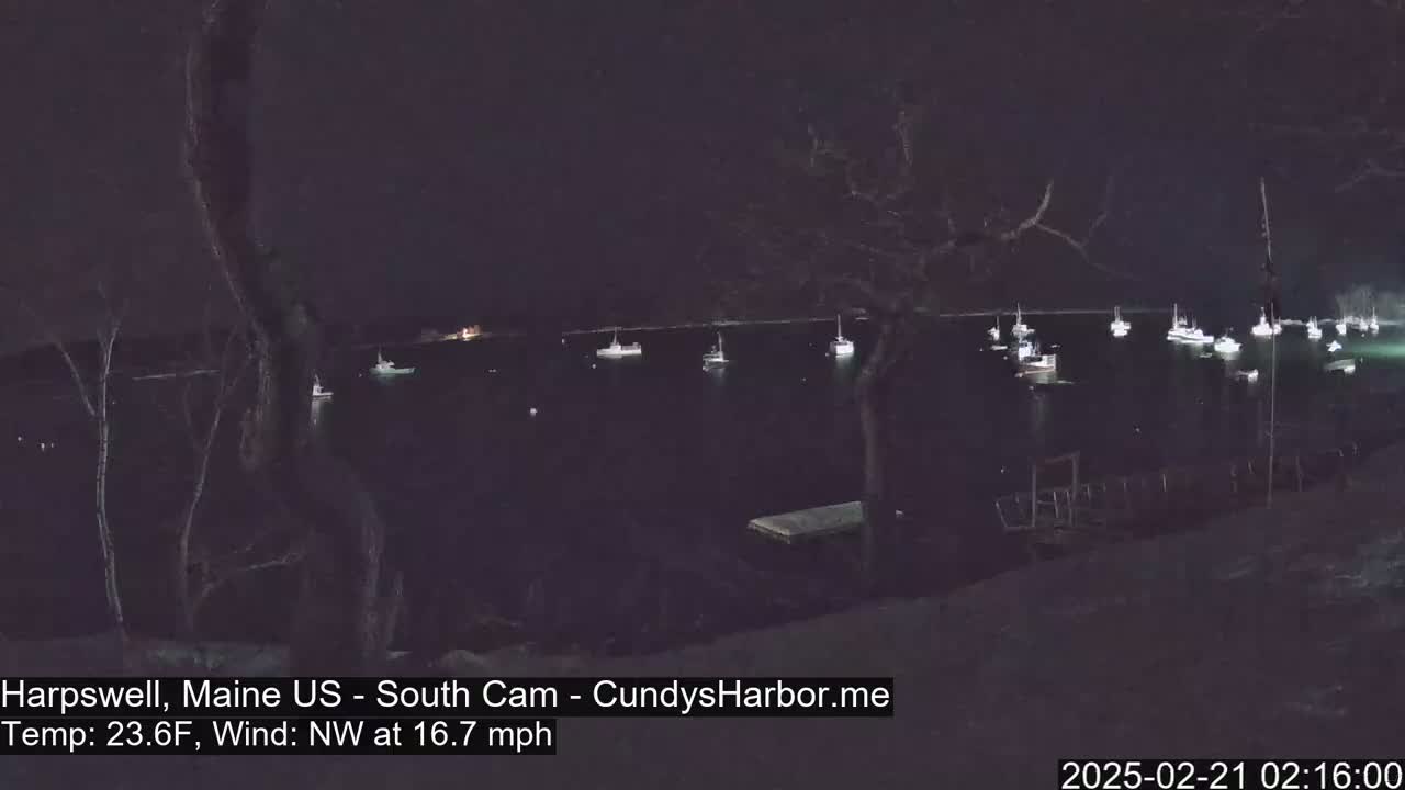 A nighttime view of a harbor with numerous boats at anchor under a dark sky, with a northwest wind.