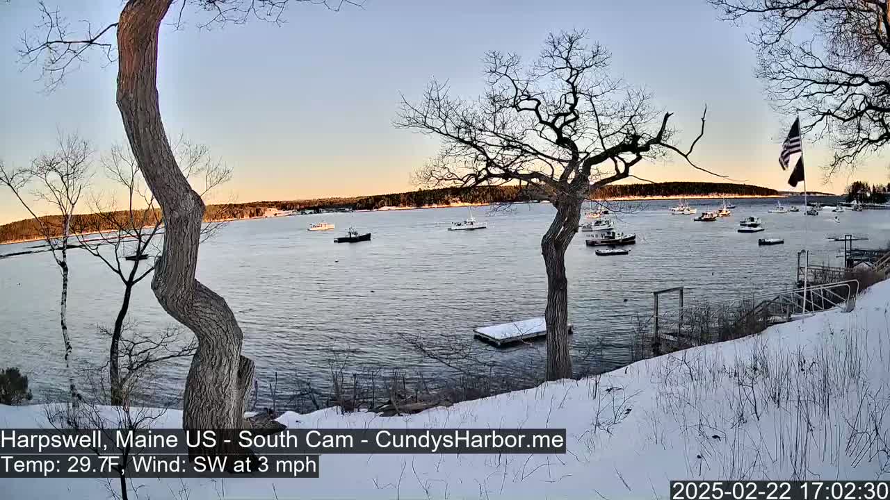 A snow-covered shoreline with several boats on calm water under a twilight sky.