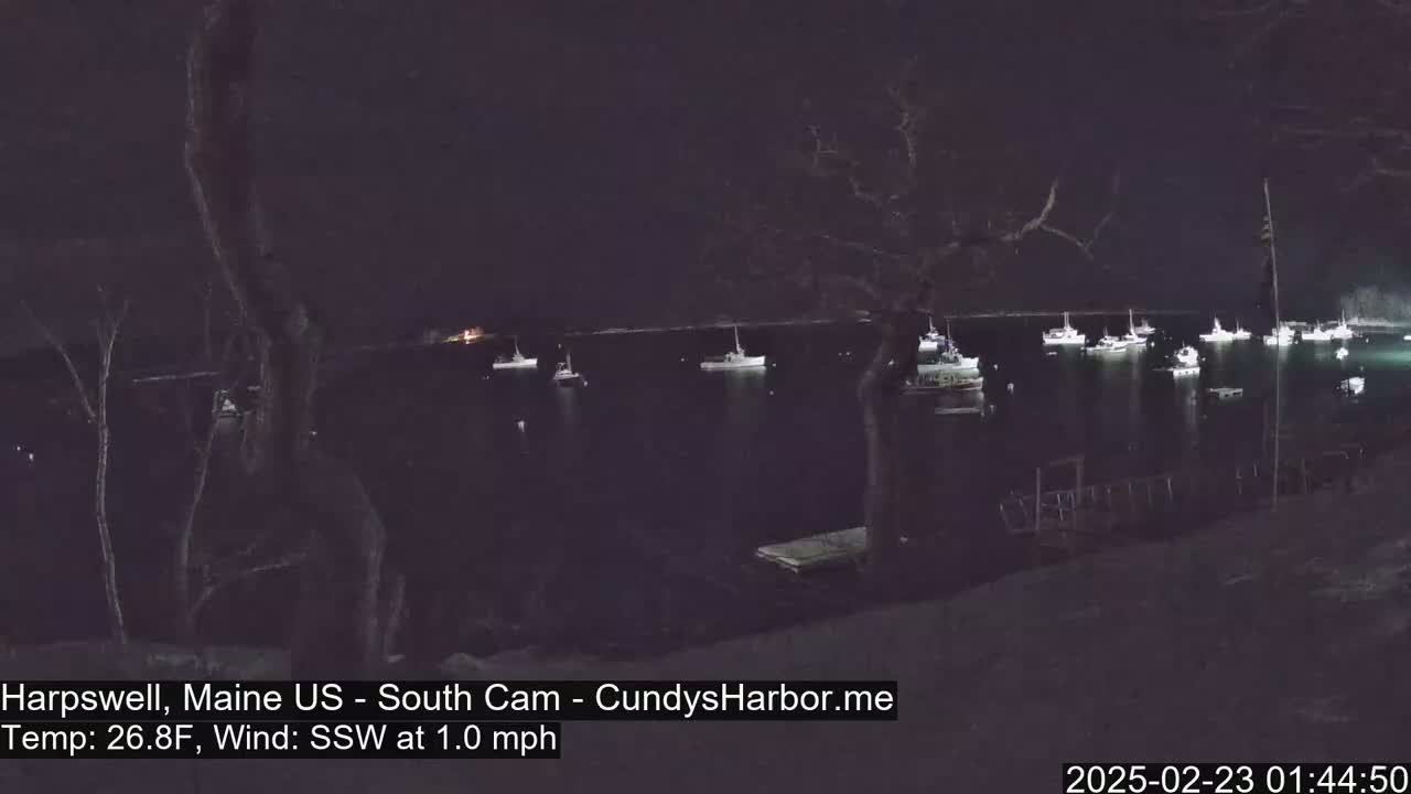 Several boats are moored in a dark harbor at night under a 26.8°F temperature with a south-southwest wind of 1.0 mph.
