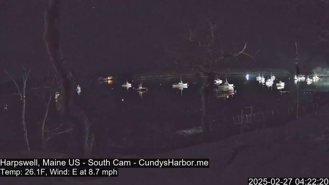 Several boats are moored in a dark harbor at night, under a clear sky with an 8.7 mph east wind and a temperature of 26.1°F.