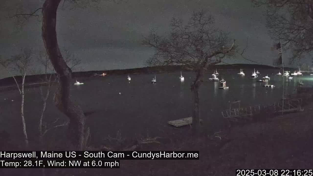 Numerous boats are moored in a dark harbor at night under a cloudy sky, with a 6 mph northwest wind and a temperature of 28.1°F.