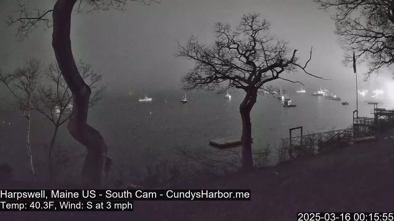 Several boats are moored in a harbor on an overcast day with a light south wind.