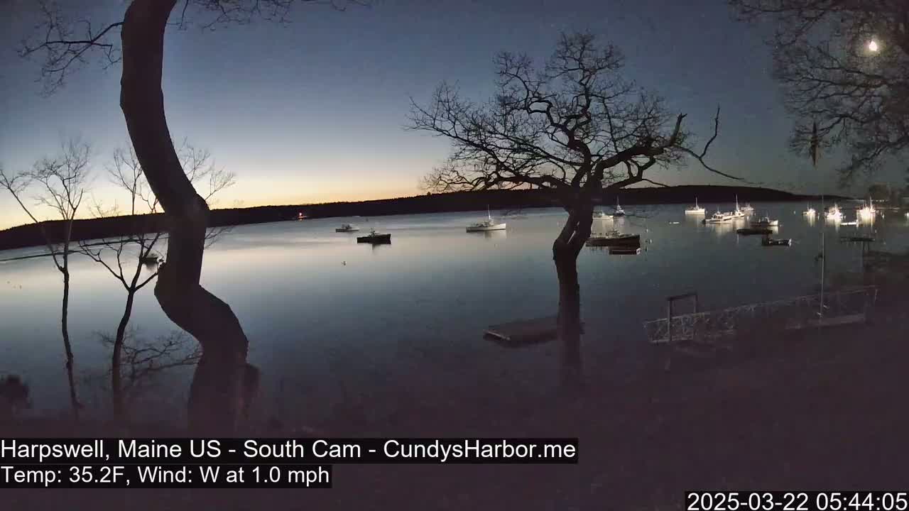 Several boats are moored in a calm harbor at twilight under a mostly clear sky.
