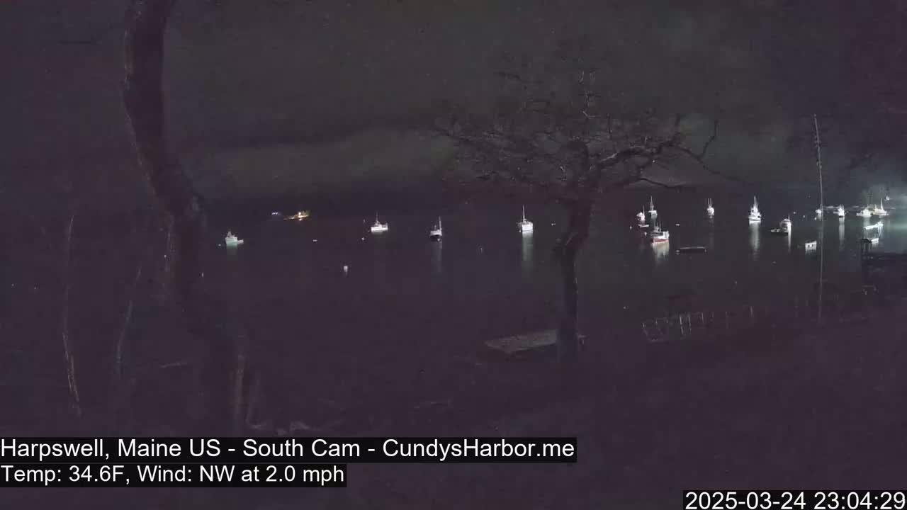 A nighttime view of several boats moored in a dark harbor under a cloudy sky with a northwest wind of 2 mph and a temperature of 34.6°F.