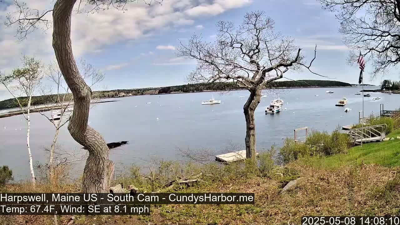 A calm bay with several boats is seen from a grassy hillside on a partly cloudy day with a southeast wind.