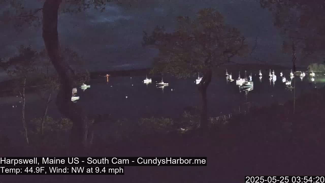 Several boats are moored in a dark harbor at night under a partly cloudy sky with a northwest wind.