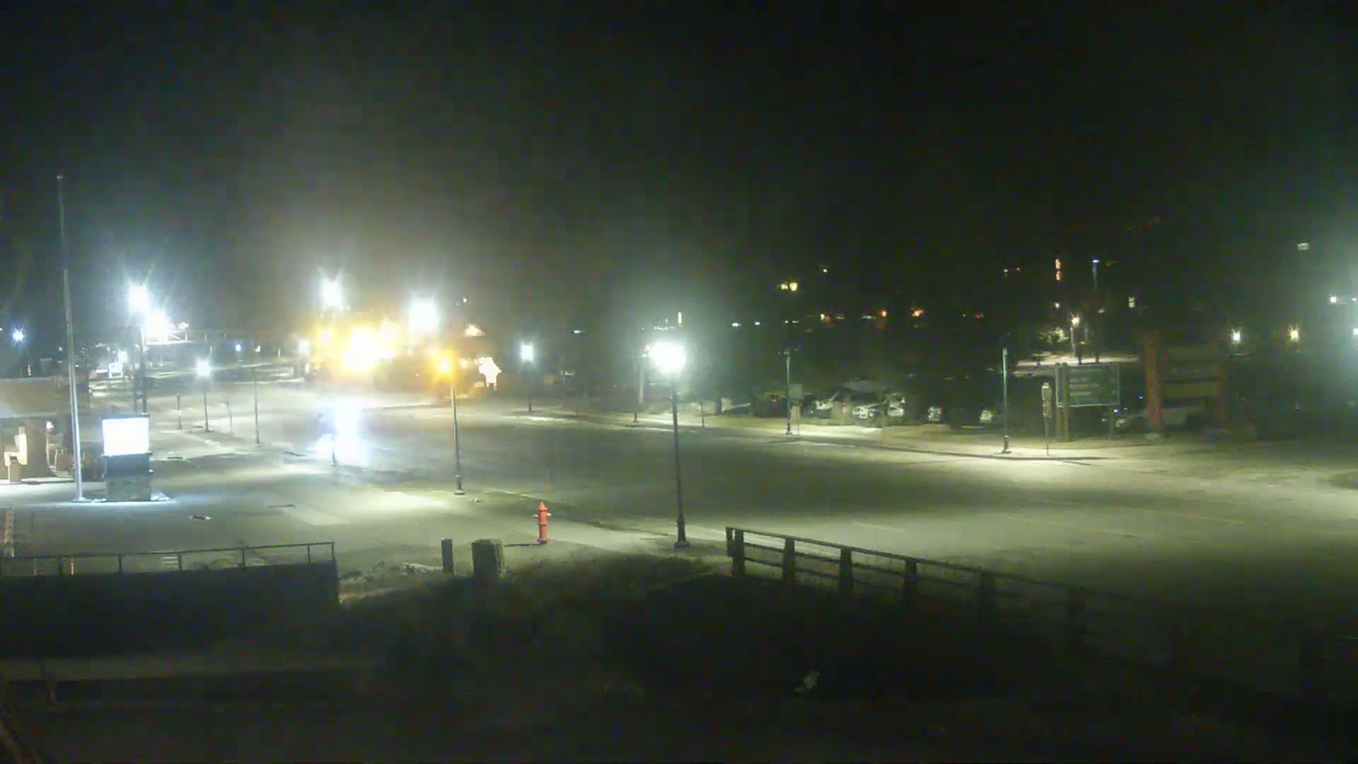 A mostly empty, brightly lit street at night, with a few vehicles visible in the distance under hazy conditions.