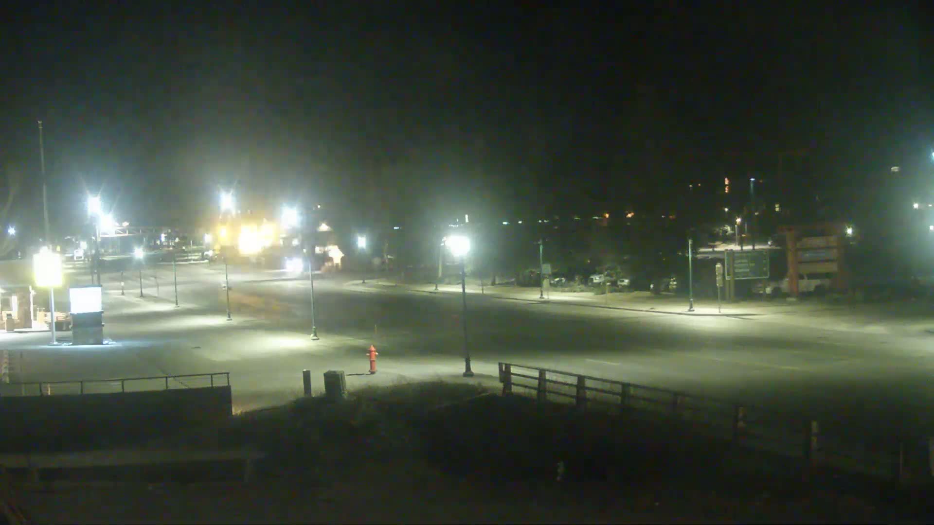 A mostly empty, well-lit road at night, with a few vehicles visible in the distance and a fire hydrant in the foreground.