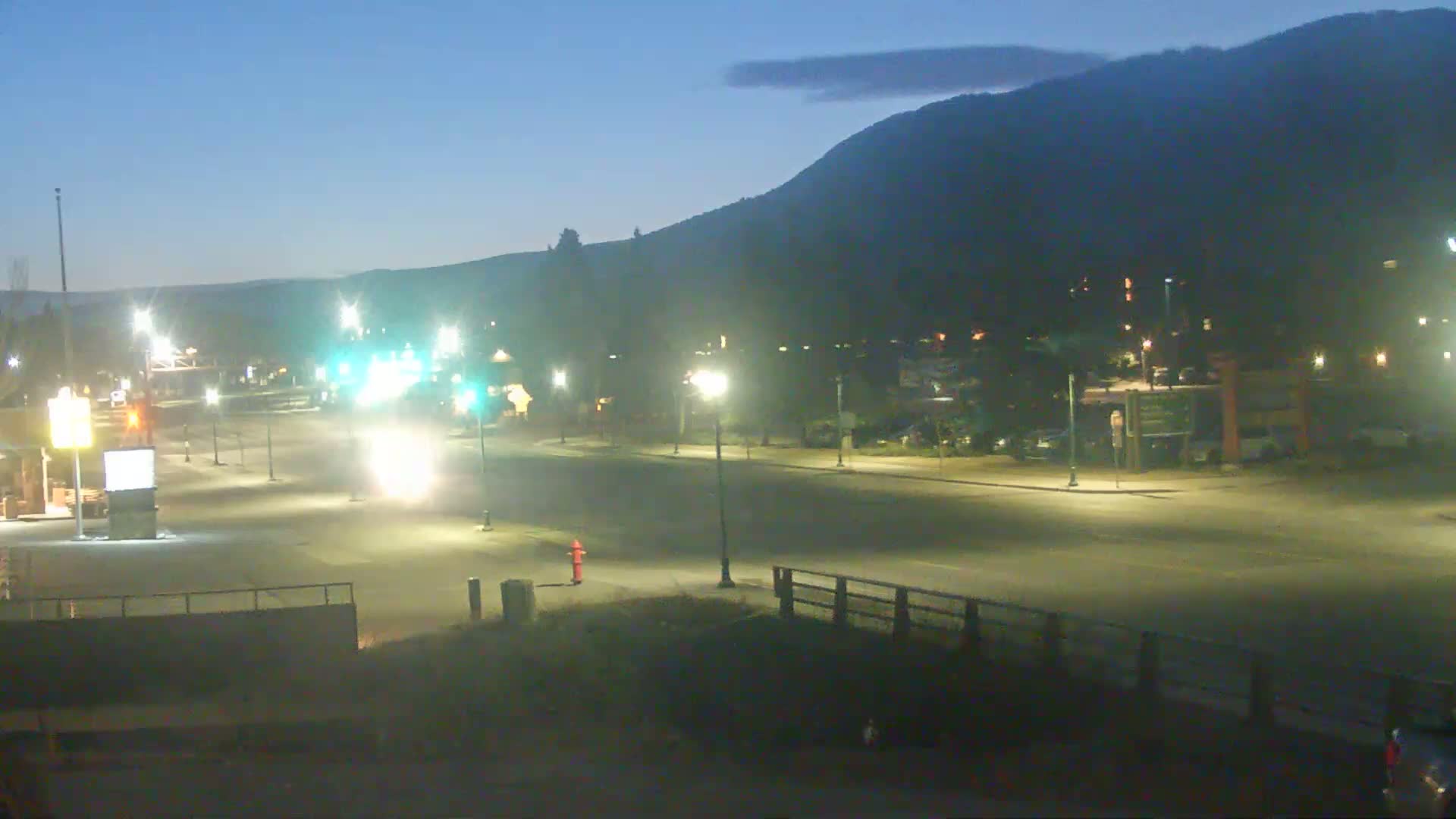 A mostly empty, well-lit road at twilight under a clear sky, with a mountain in the background.