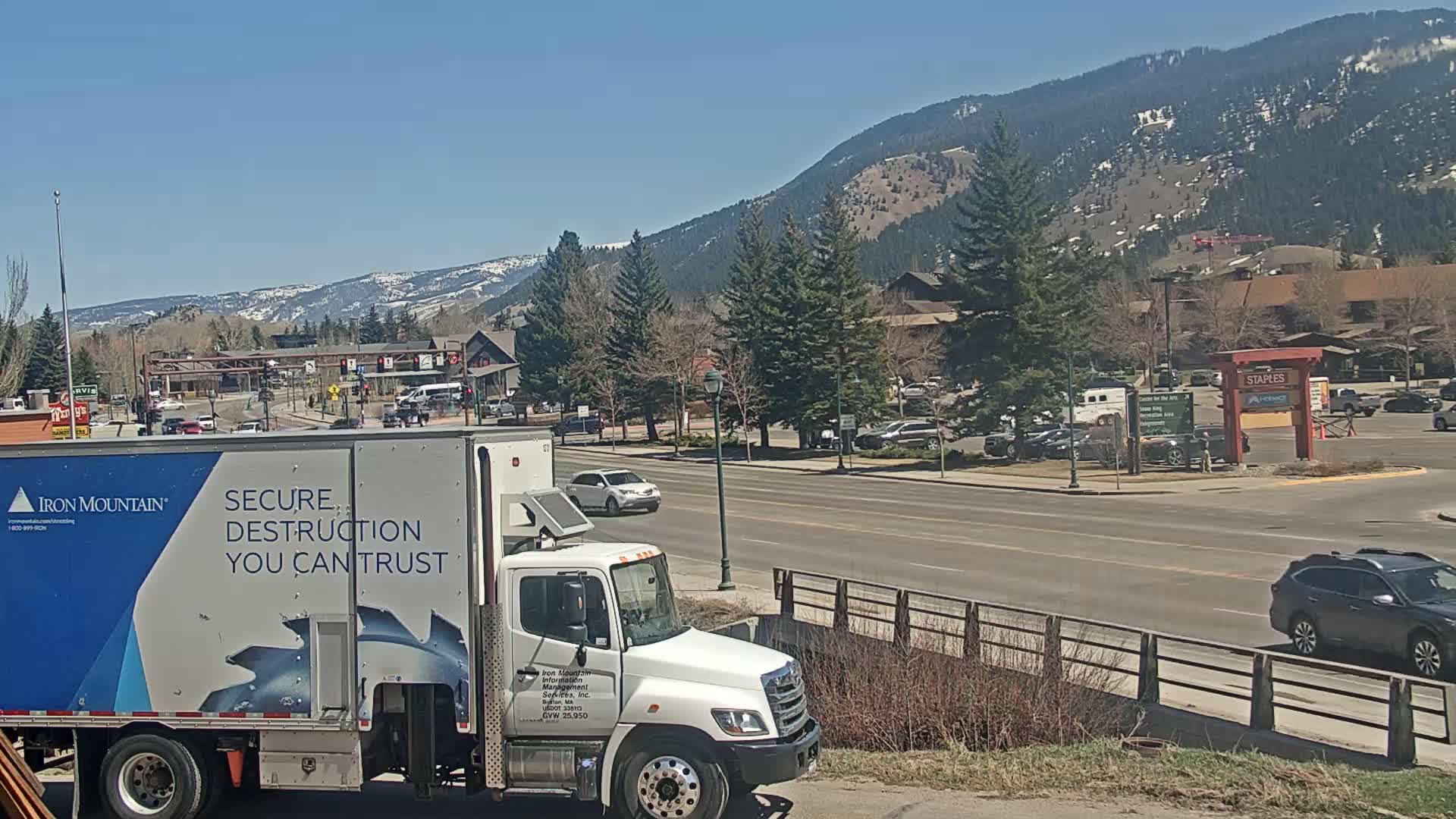 A white truck with a blue logo and the words "Secure Destruction You Can Trust" is parked on a street in front of a mountain range on a sunny day.