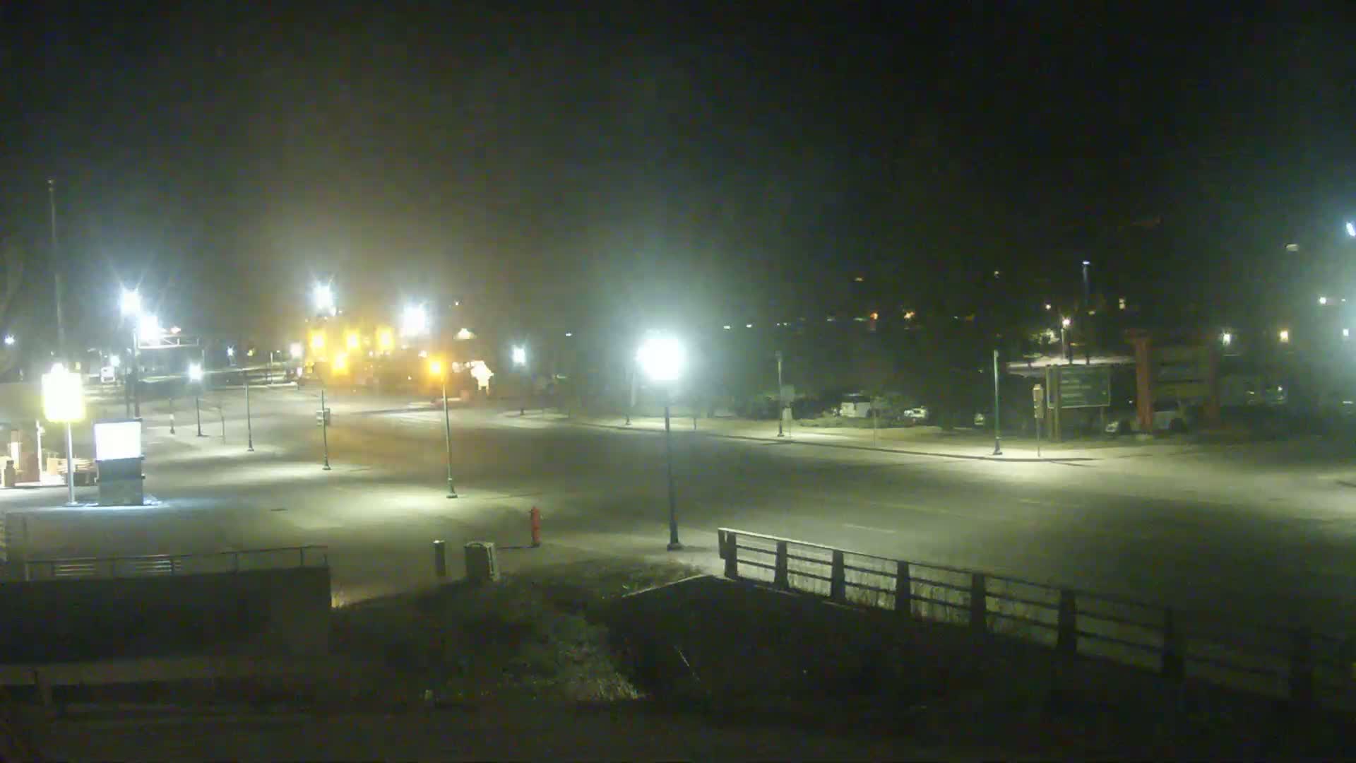 A mostly empty roadway at night, illuminated by streetlights, with a hazy or foggy atmosphere.