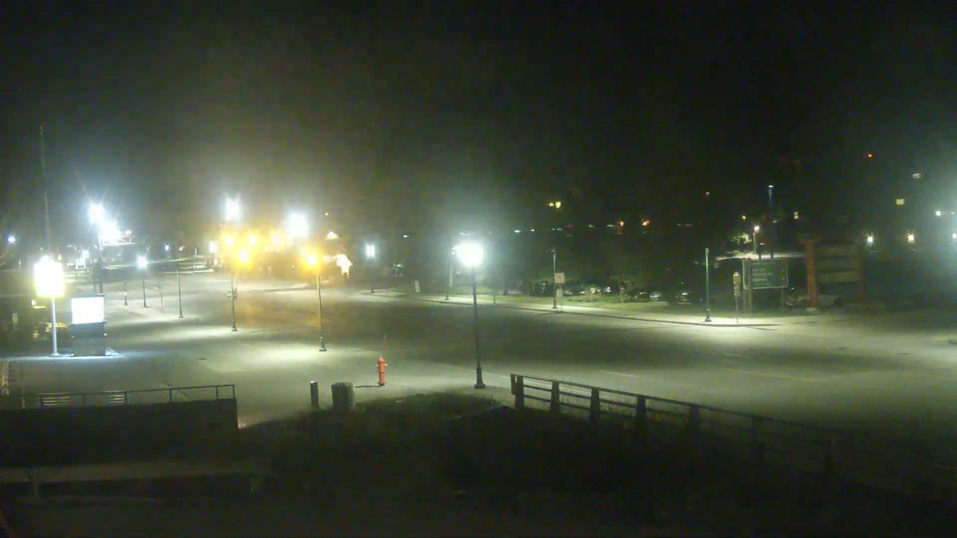 A mostly empty, well-lit roadway at night with some haze or fog in the air.