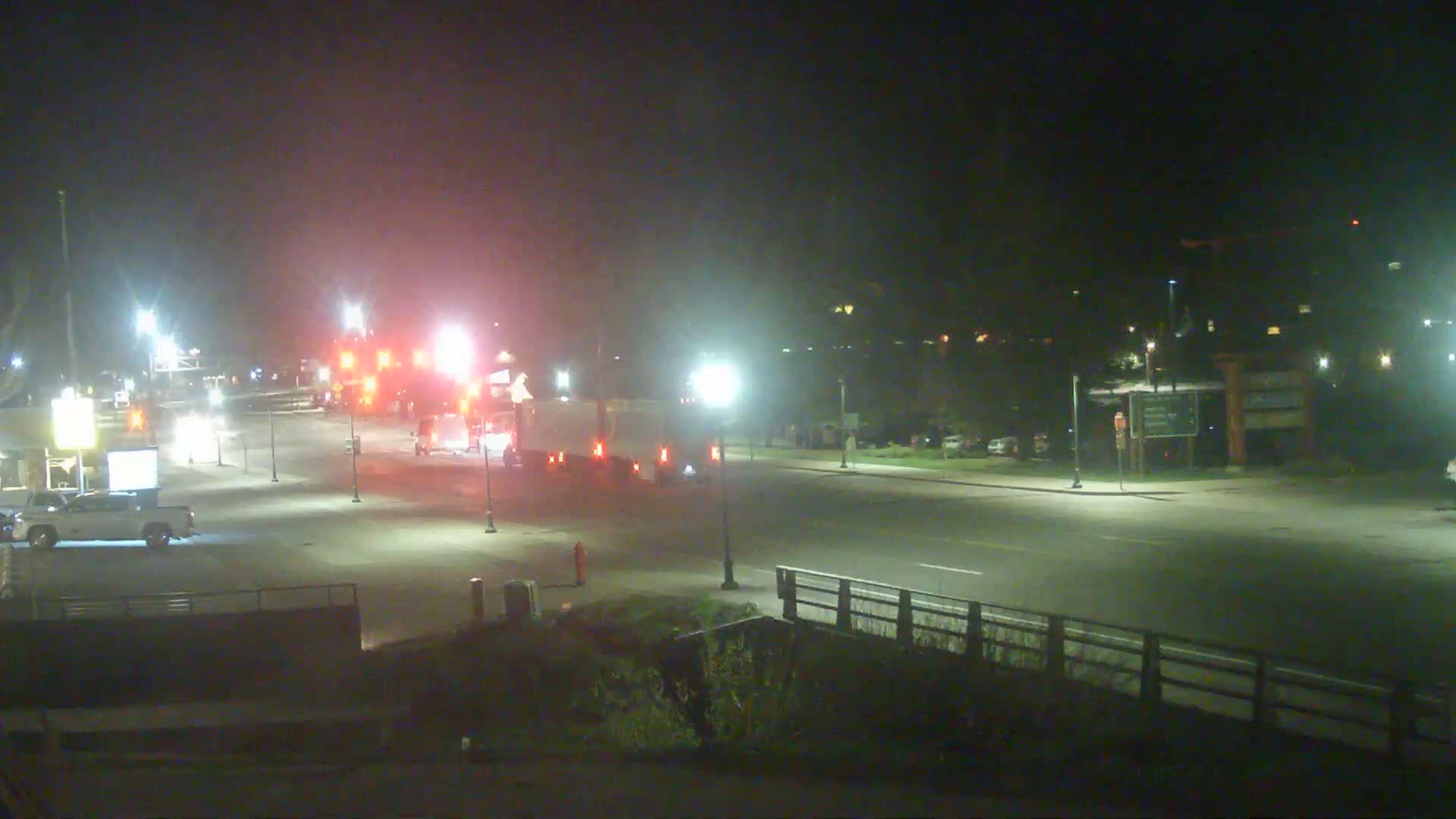 At night, emergency vehicles and a large truck are stopped on a roadway illuminated by streetlights.