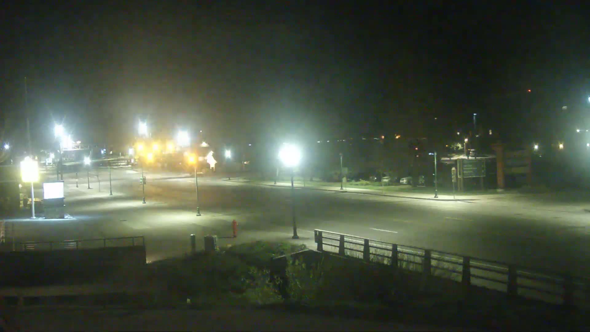 A nighttime view of a mostly empty road with streetlights and some distant vehicles under hazy conditions.
