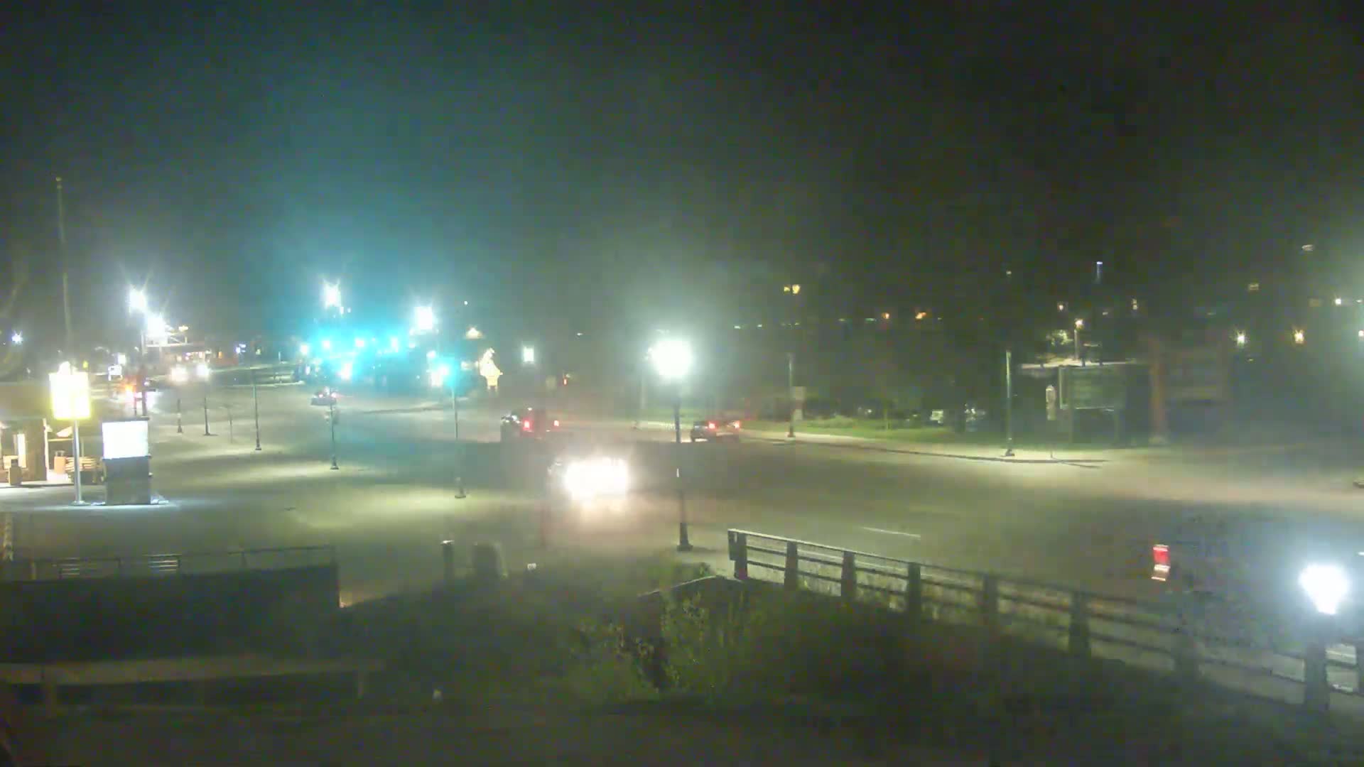A nighttime view of a sparsely trafficked intersection with several streetlights illuminating the road and surrounding area.