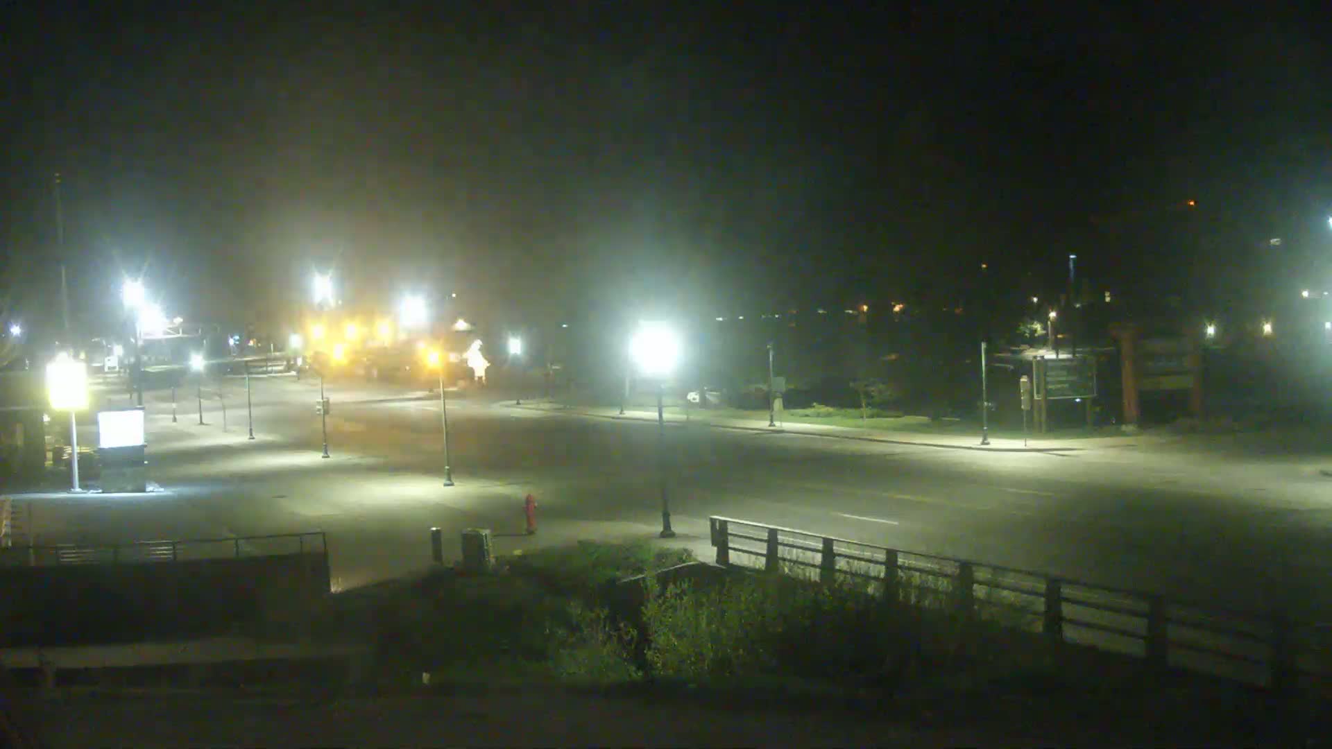 A nighttime, hazy view of a mostly empty road lit by streetlights, with some vehicles visible in the distance.