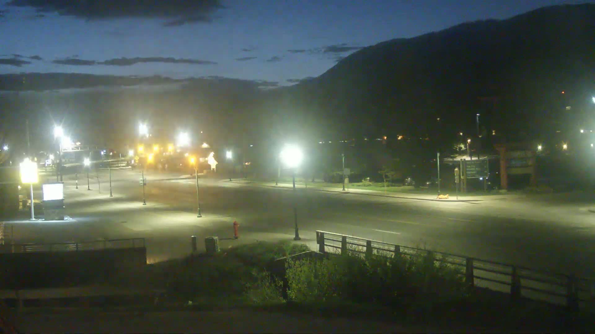 A mostly empty, well-lit roadway at night under a dark, clear sky, with a mountain in the background.