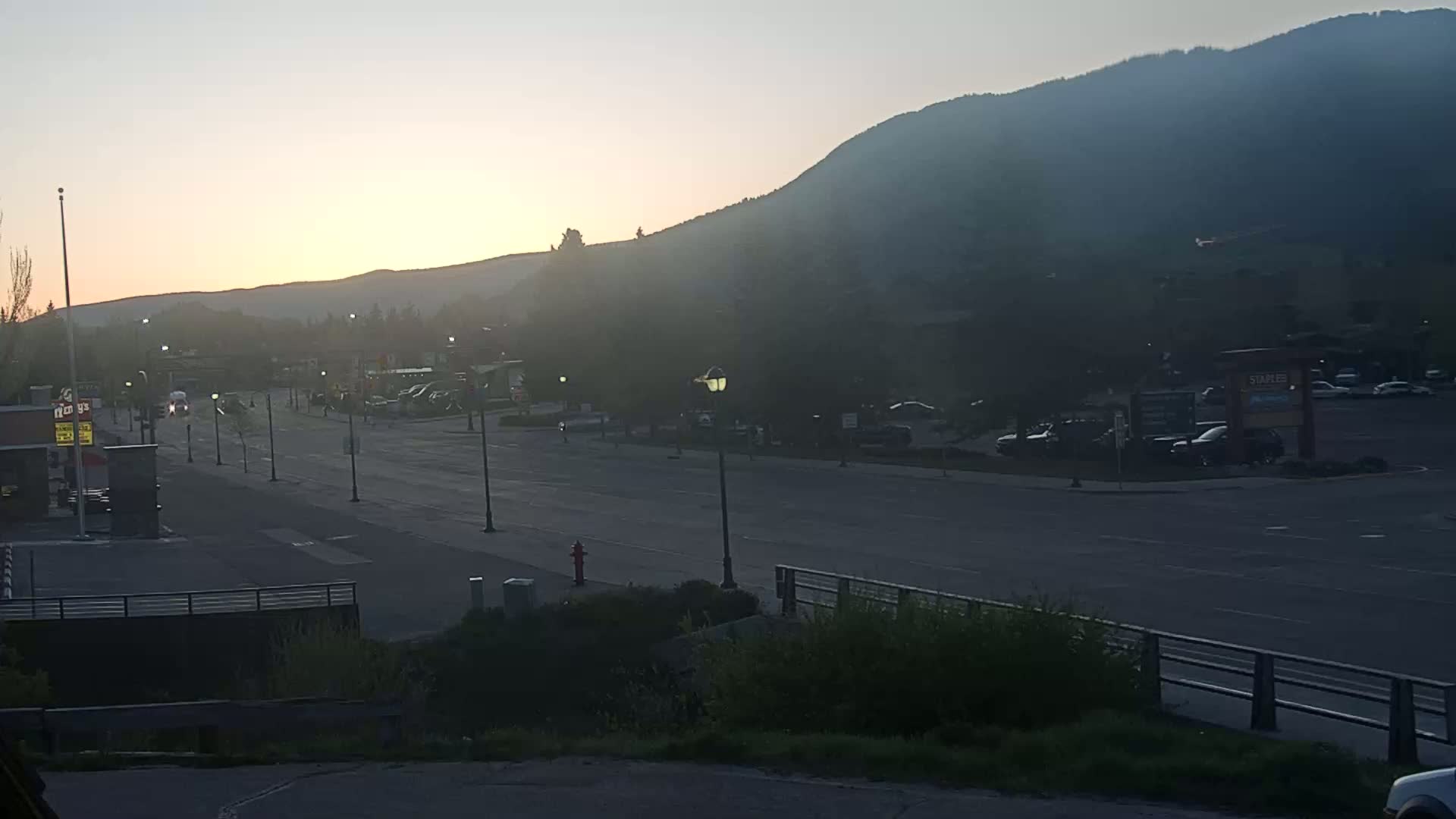 A mostly empty street at sunrise is seen beneath a hazy mountain range.